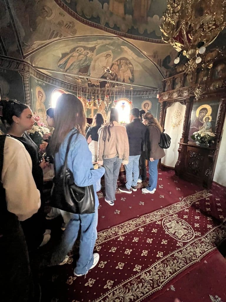 Elevi în biserică, în fața icoanelor de pe peretele pictat