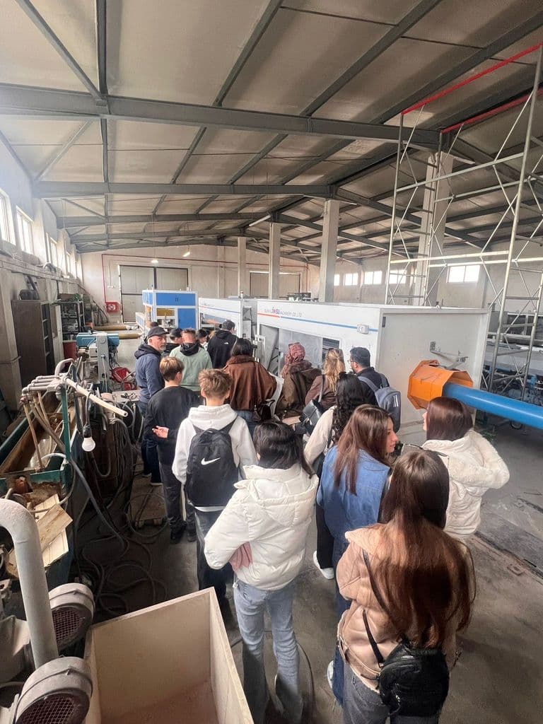 Elevii adunați în jurul unei linii de producție, în hala fabricii