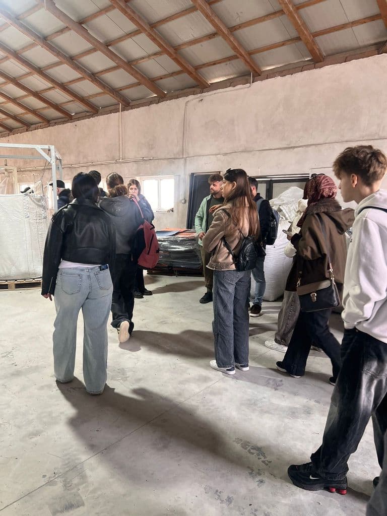 Grup de vizitatori în hala industrială, lângă saci mari de materie primă