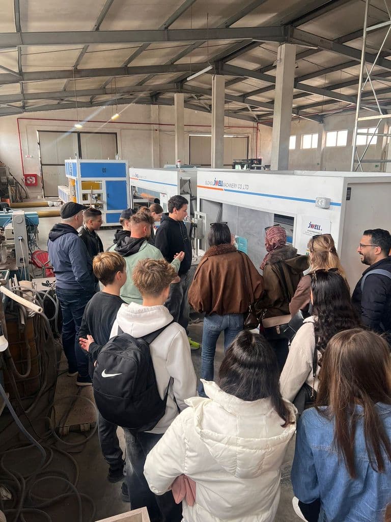 Elevii urmăresc explicațiile în hala de producție, lângă utilaje