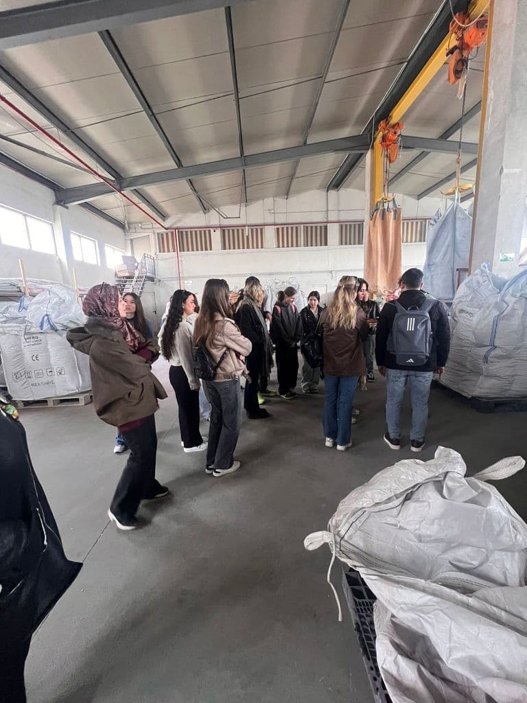 Grup de elevi în hala fabricii, printre saci mari de material